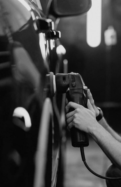 Un Carrossier se sert d'une ponceuse pour réparer la carrosserie d'une voiture. Photo illustrant le service Carrosserie fournit par la Carrosserie Jambu.