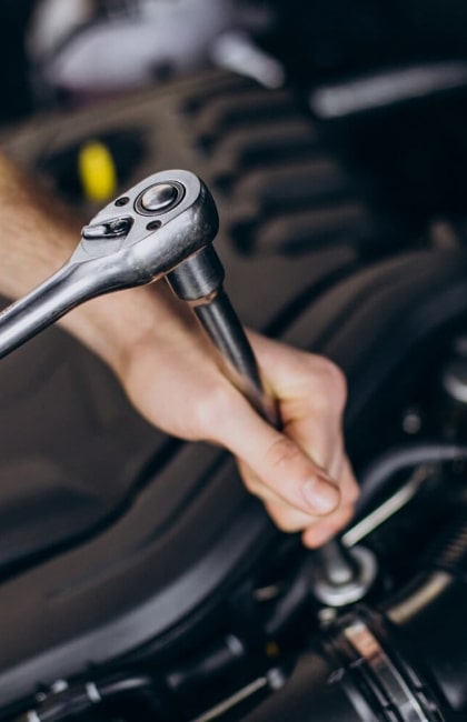 La main d'un carrossier mécanicien utilise une clé à molette pour entretenir une voiture. Photo illustrant le service Mécanique proposé à la Carrosserie Jambu.
